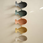 Two sets of stacked whale-shaped bath toys in muted, earthy tones resting on a neutral surface with soft lighting.