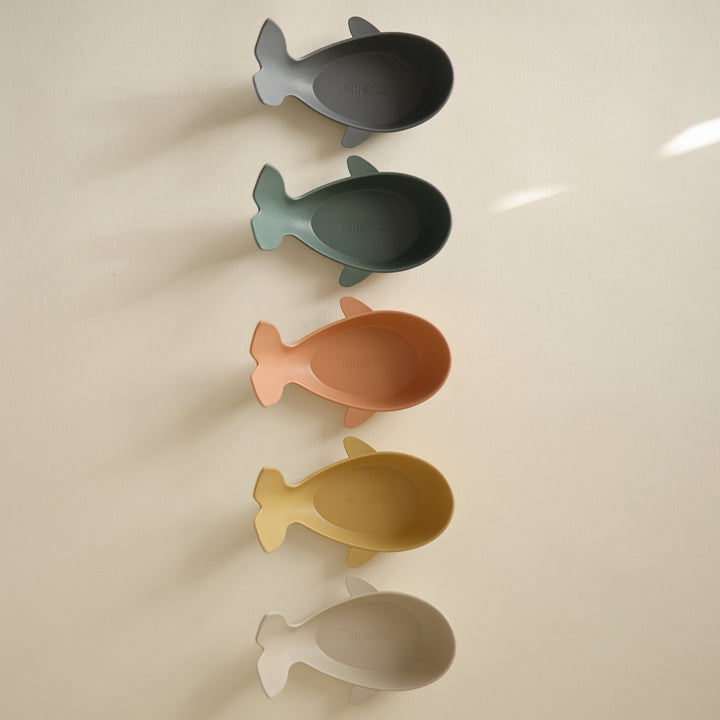Two sets of stacked whale-shaped bath toys in muted, earthy tones resting on a neutral surface with soft lighting.