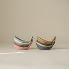 Two sets of stacked whale-shaped bath toys in muted, earthy tones resting on a neutral surface with soft lighting.
