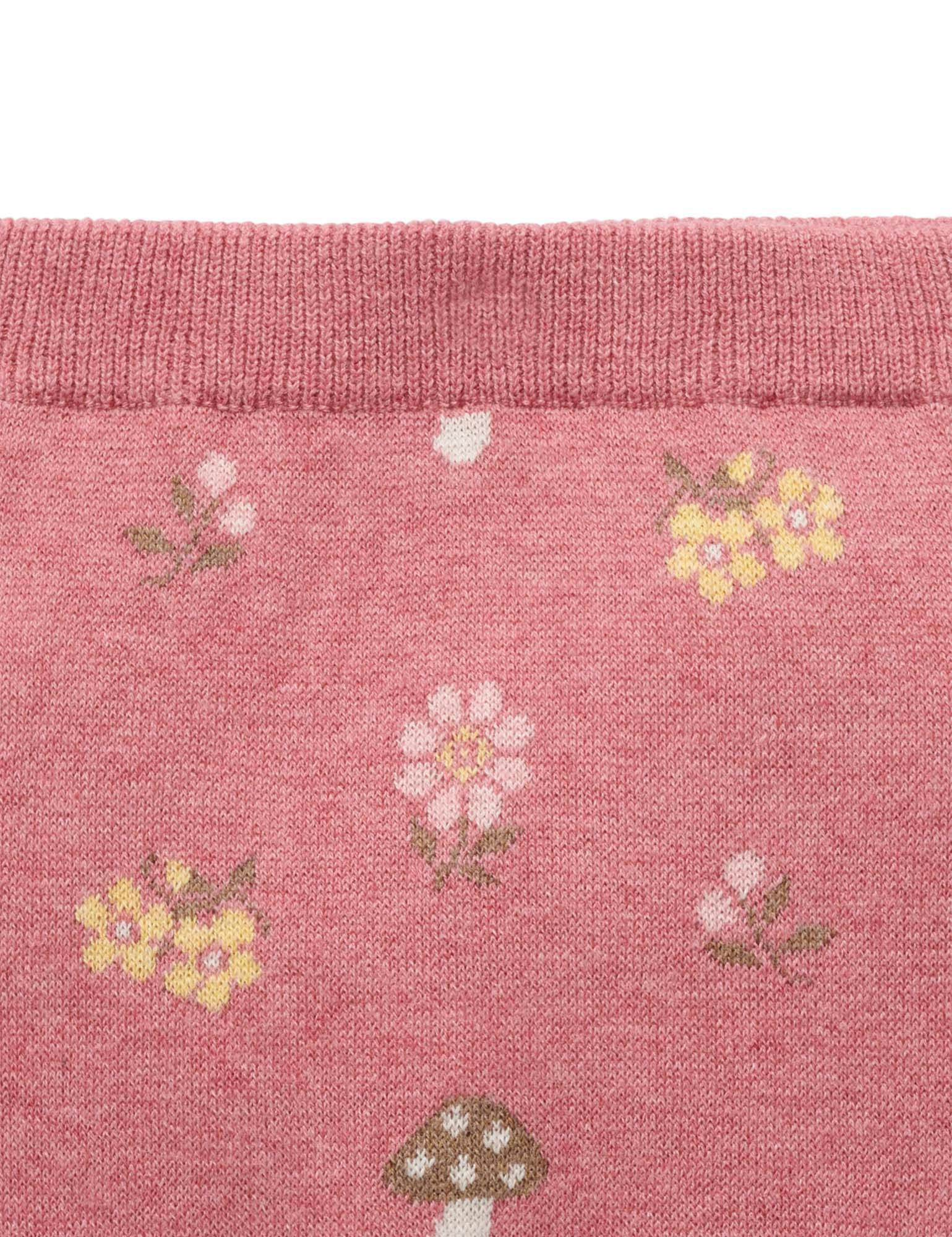 Close-up of a pink knit fabric with a repeating pattern of small flowers and mushrooms, showing a ribbed cuff at the top.