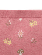 Close-up of a pink knit fabric with a repeating pattern of small flowers and mushrooms, showing a ribbed cuff at the top.