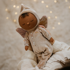 Baby doll in a beige outfit with a hood and ears against a soft, blurred background with lights.