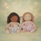 Two dolls with different skin tones sitting side by side on a soft, blurred background.