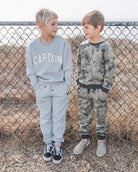 Two children wearing matching outfits in front of a chain-link fence.