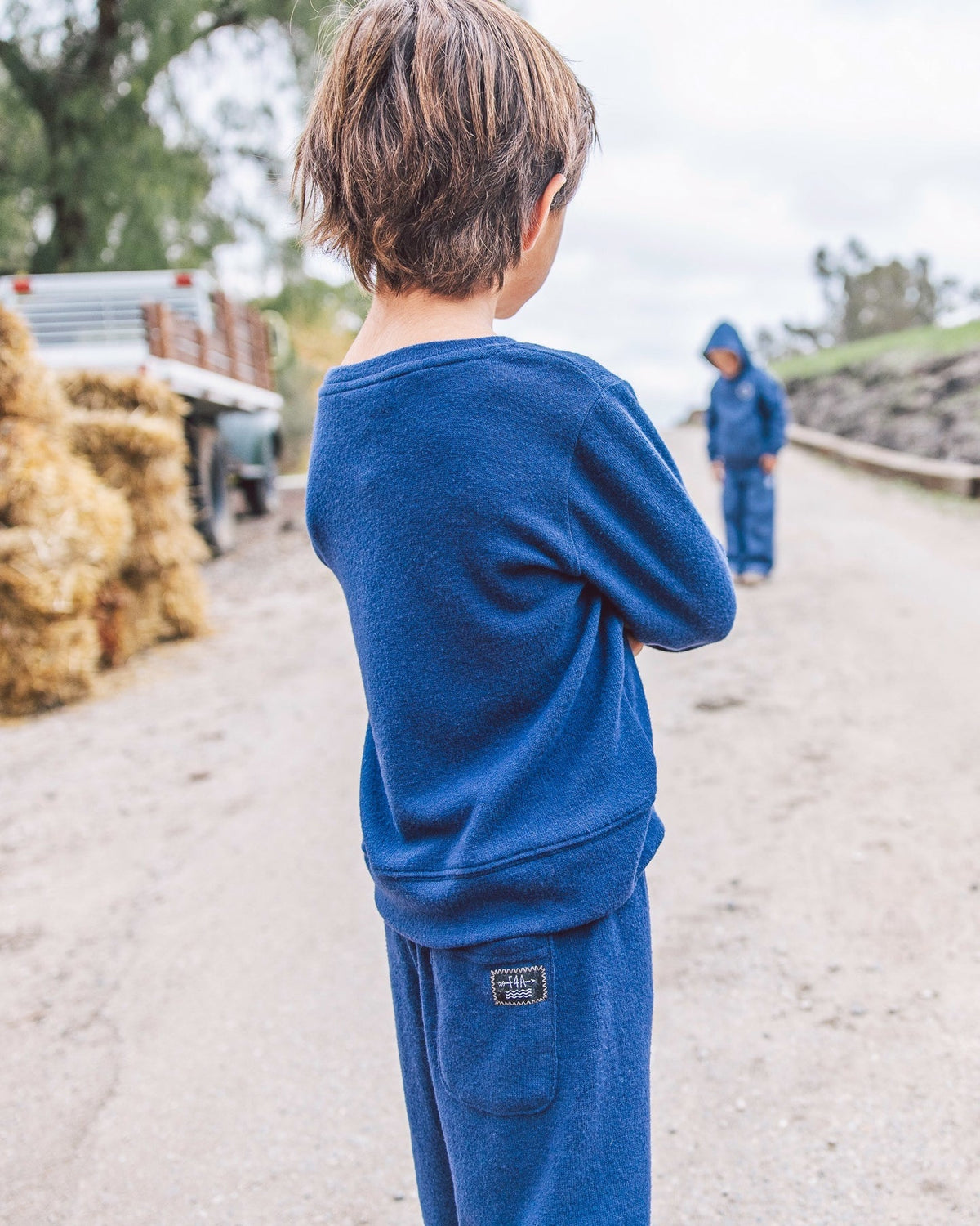 A child wearing a matching navy blue sweatshirt and sweatpants set, viewed from behind on an outdoor dirt path.