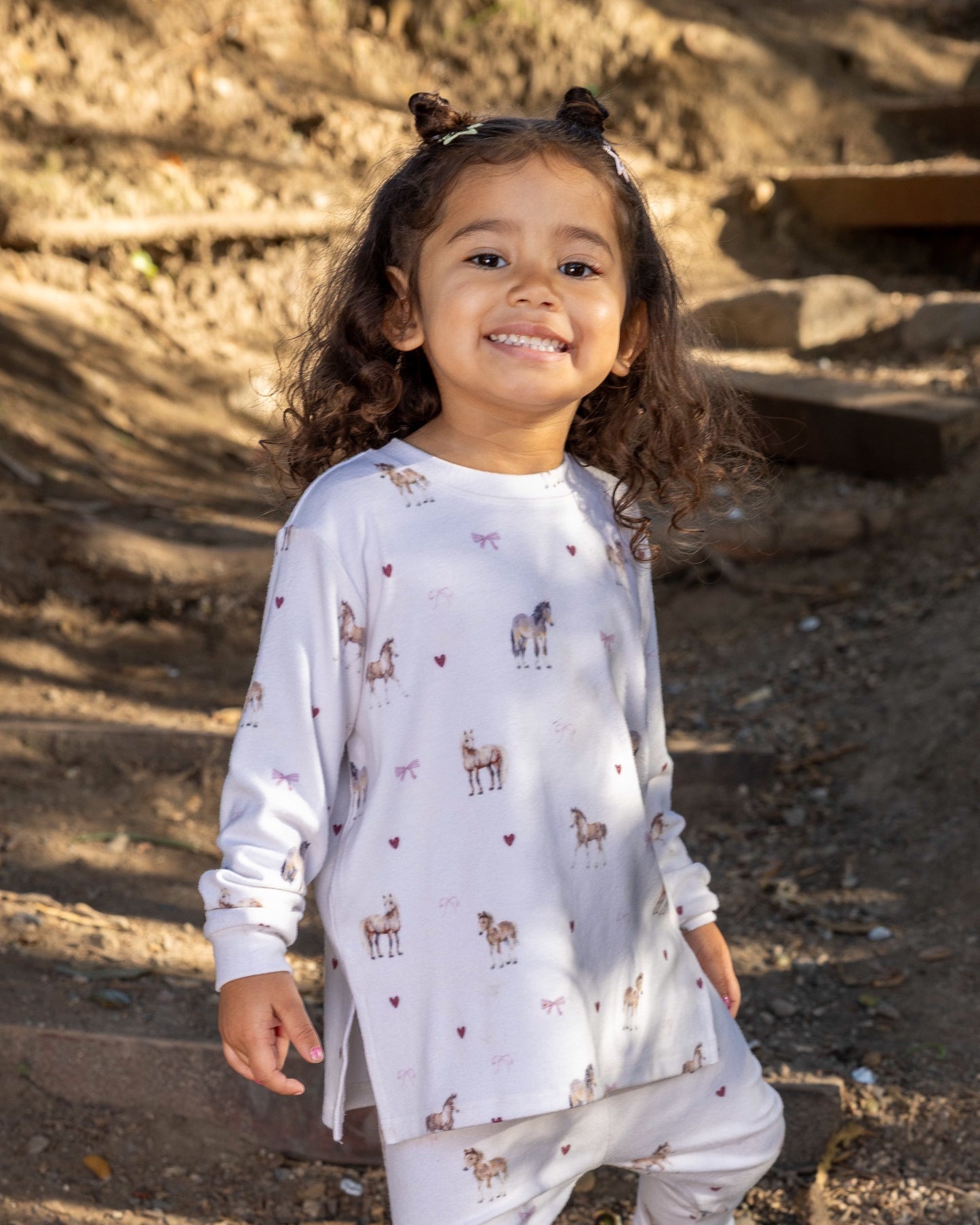 A young child wearing a white long-sleeve pajama top and matching pants with a deer print, standing outdoors on stone steps.