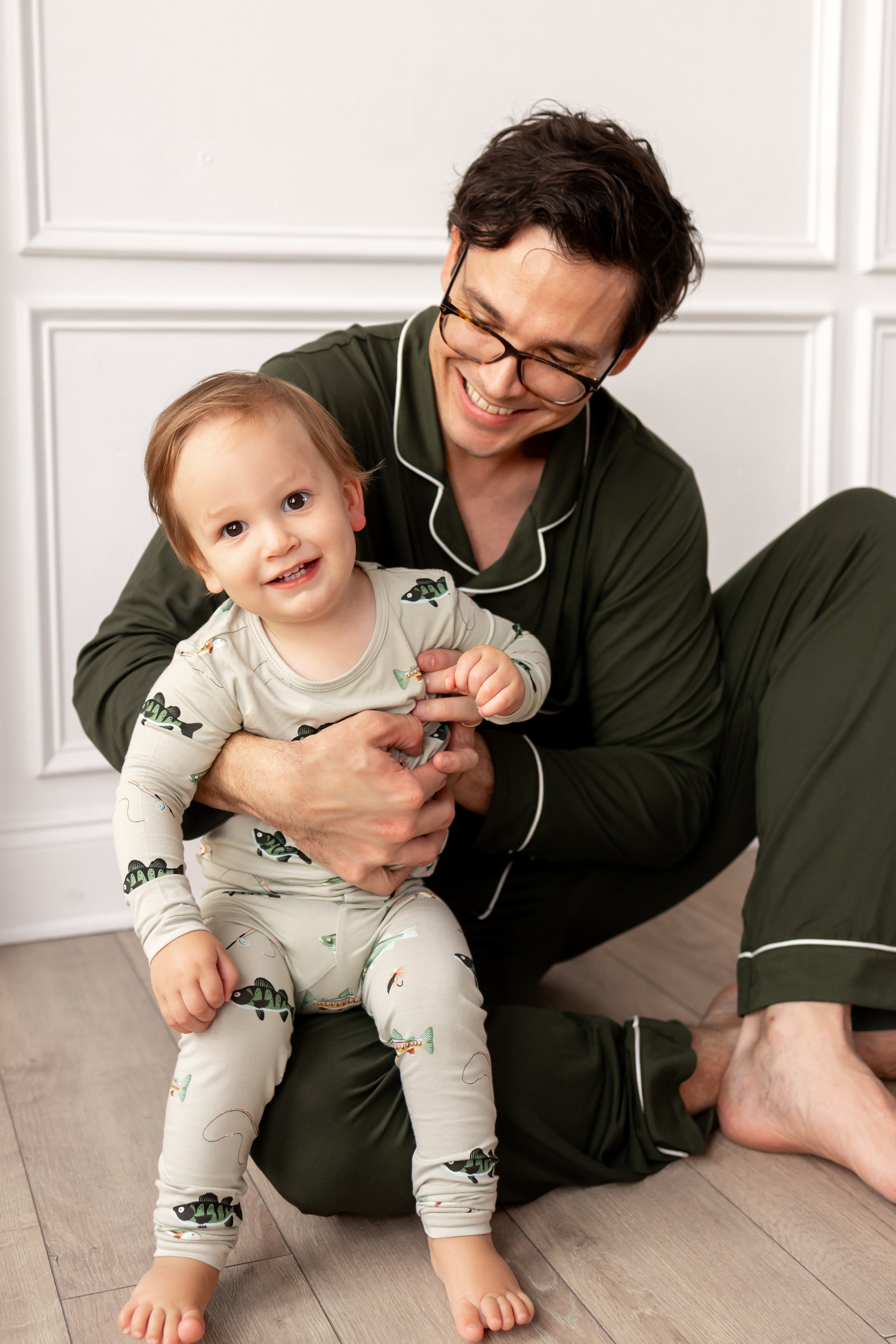 Man and child in matching pajamas sitting on a wooden floor.