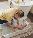 Woman washing a baby in a bathtub on a bathroom floor.