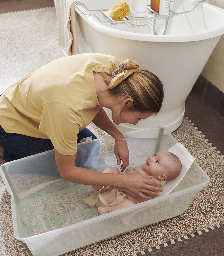 Woman washing a baby in a bathtub on a bathroom floor.