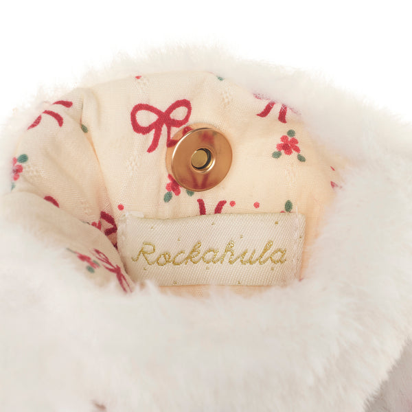 Close-up of a plush white faux-fur trim with a cream fabric lining printed with red bows and small red floral motifs, featuring a gold snap button and a visible Rockahula brand label.