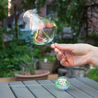 Hand holding a bubble wand with a bubble, set against a garden background