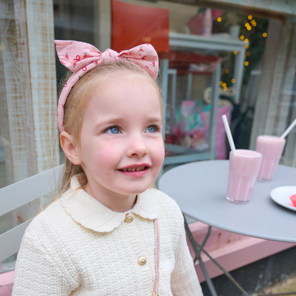 Young girl with a pink bow in her hair sitting at a table with pink drinks.
