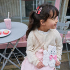 Young girl holding a plush toy with a pink chair and table in the background