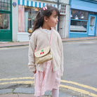 Young girl with a gold purse with cherry design standing on a street.
