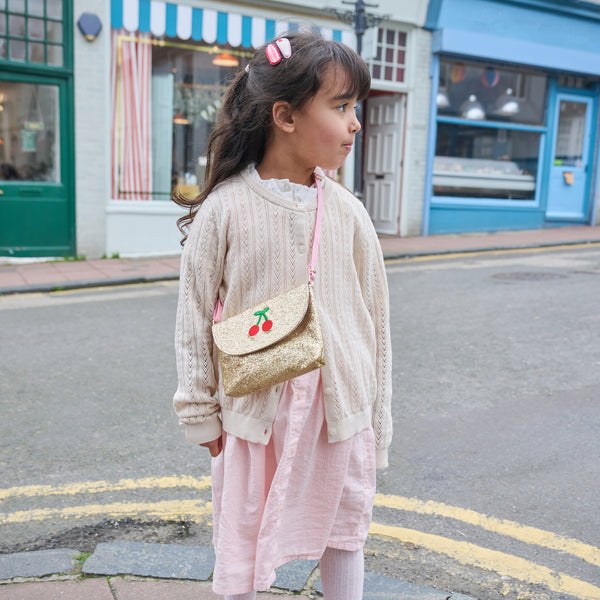Young girl with a gold purse with cherry design standing on a street.
