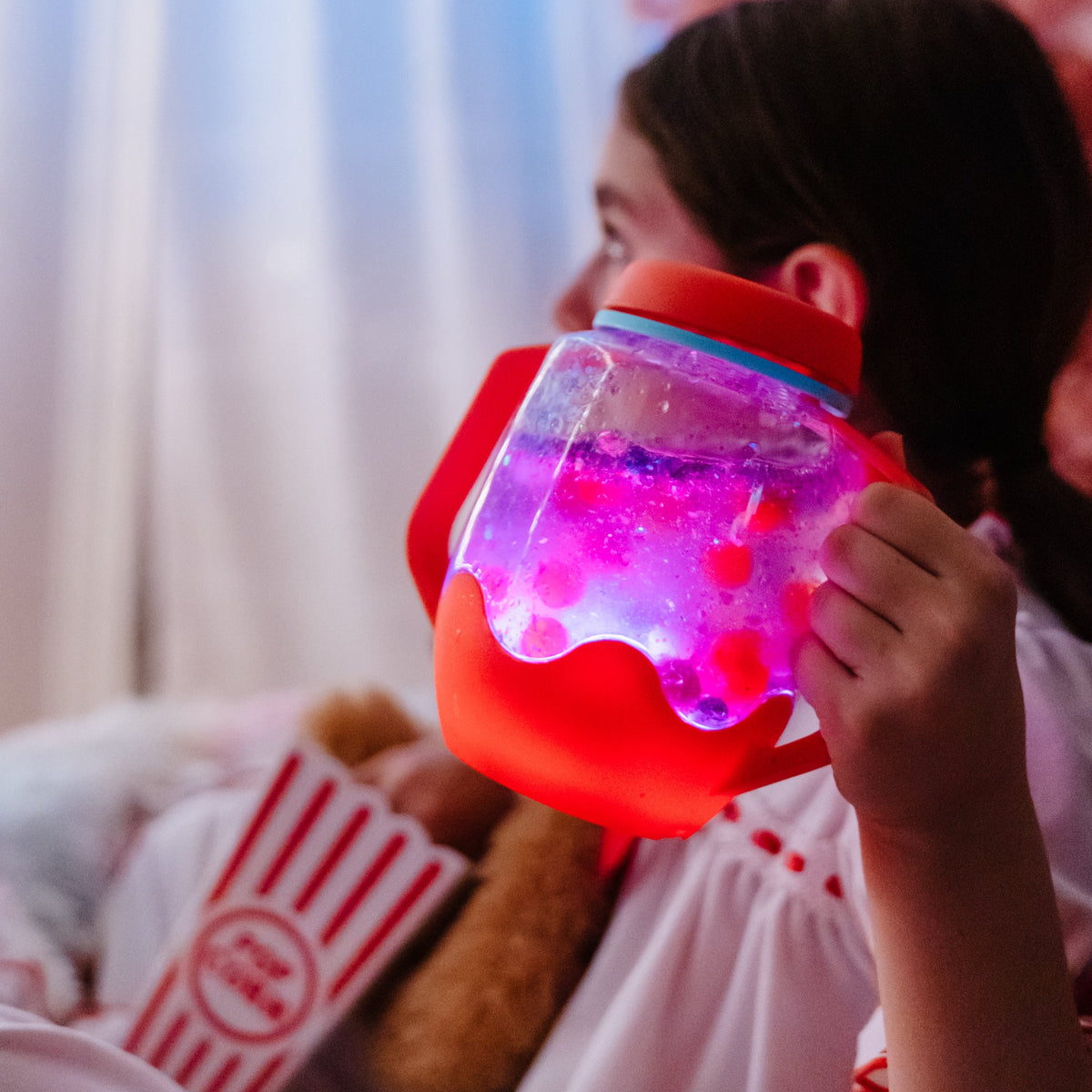 Child holding a colorful light-up jar with a soft toy and box in the background