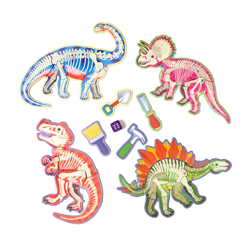 Colorful dinosaur fossil puzzle pieces and excavation tools from the Dinosaur Dice Game by Eeboo, featuring a T-Rex, Triceratops, Stegosaurus, and Brontosaurus skeleton.