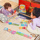 Two children playing with colorful cards on the floor next to a red toy chest.