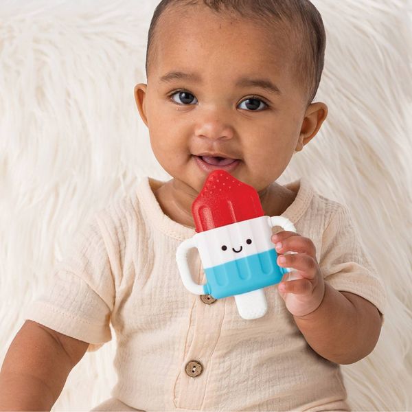 Baby holding a blue and red toy resembling a popsicle on a white background