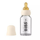 Glass baby bottle with beige cap and nipple on a white background
