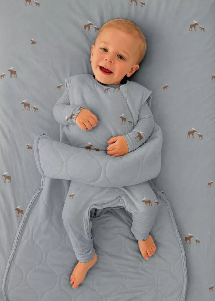 A baby lying on a patterned gray blanket, wearing a matching gray quilted swaddle wrap around the body and legs.