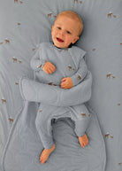A baby lying on a patterned gray blanket, wearing a matching gray quilted swaddle wrap around the body and legs.