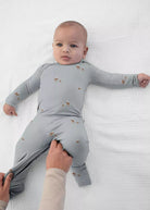 A baby wearing the günamüna Woof Sage Convertible Footie Pajama featuring an all-over small dog print.