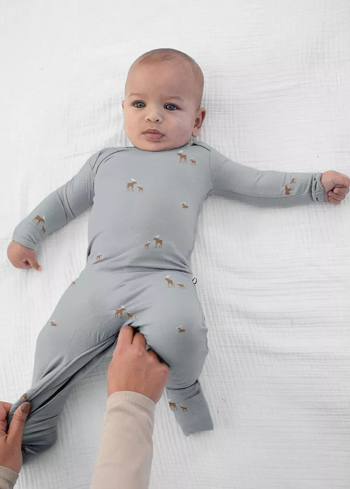 A baby wearing the günamüna Woof Sage Convertible Footie Pajama featuring an all-over small dog print.