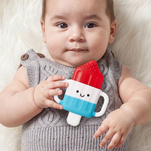 Baby holding a colorful popsicle-shaped toy with a neutral background