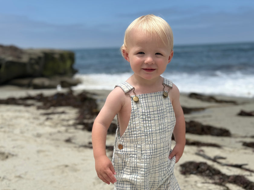 Child in a checkered dress standing on a beach with ocean in the background