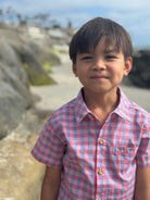 Child wearing a red and blue checkered shirt standing outdoors with rocks and sky in the background