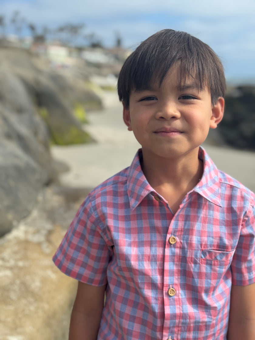 Child wearing a red and blue checkered shirt standing outdoors with rocks and sky in the background