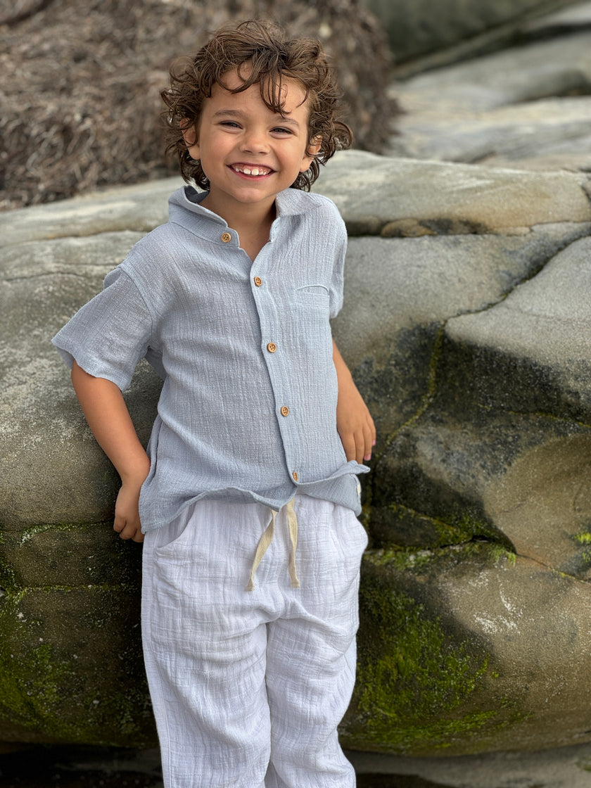 Child wearing a light blue outfit standing on rocks with a natural background