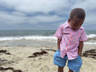 Child in a checkered shirt and shorts standing on a beach with ocean waves in the background