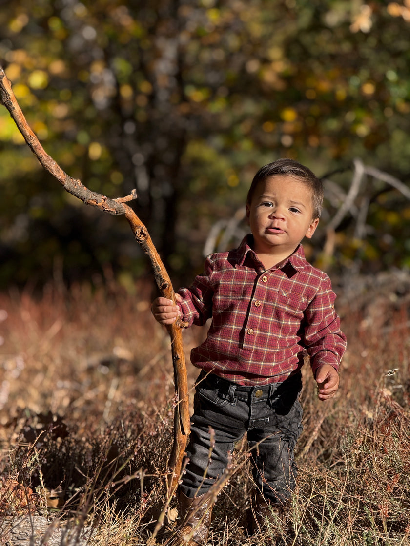 Child holding a stick in a natural setting with trees and dry grass.