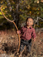 Child holding a stick in a natural setting with trees and dry grass.