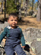 Child in denim overalls sitting on rocks in a forest