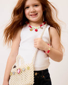 Young girl holding a pearl-handled bag with decorative elements on a plain background