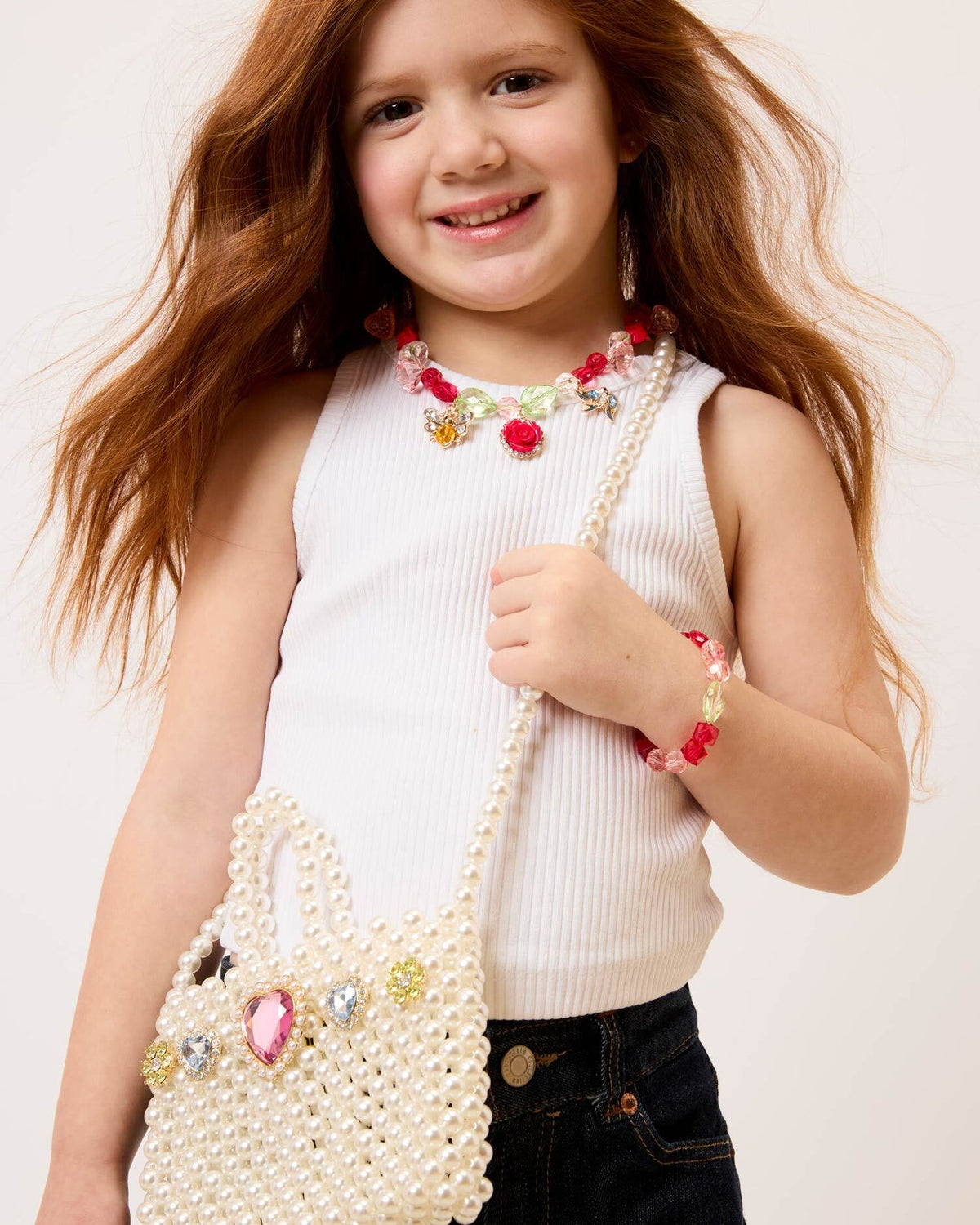 Young girl holding a pearl-handled bag with decorative elements on a plain background