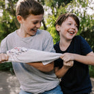 Two children holding a white shirt outdoors with greenery in the background