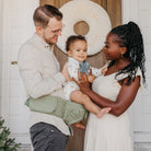 Family of three standing in a doorway with a decorative wreath, one person holding a baby.