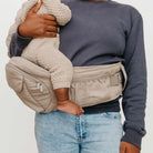 Person holding a baby in a beige baby carrier against a plain background