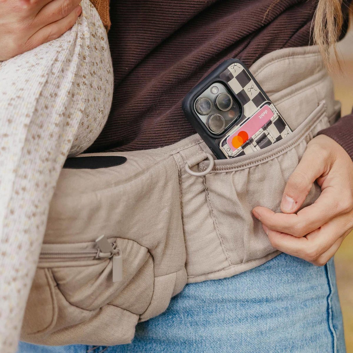 Person wearing a beige jacket with a phone case featuring a checkered pattern and Mastercard logo.