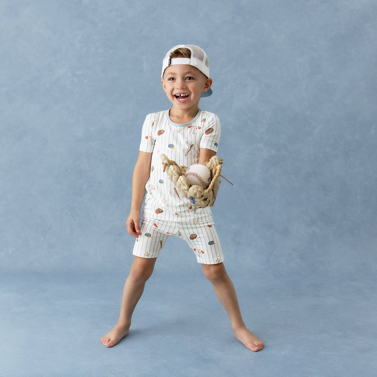 Child wearing a baseball-themed outfit with a cap, holding a baseball and glove against a blue background