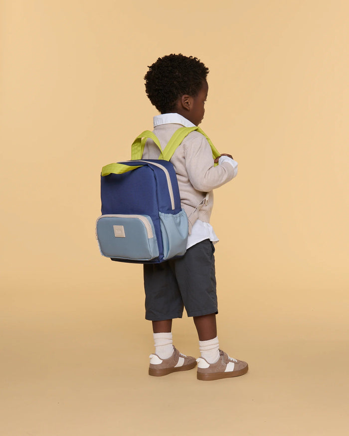 Child wearing a blue and gray backpack with green straps on a beige background