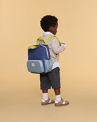 Child wearing a blue and gray backpack with green straps on a beige background