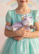 Child in a sparkly dress holding a plush unicorn toy with a rainbow in the background