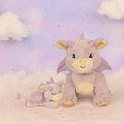 Two plush dragon toys on a soft, cloud-like surface with a pastel background.
