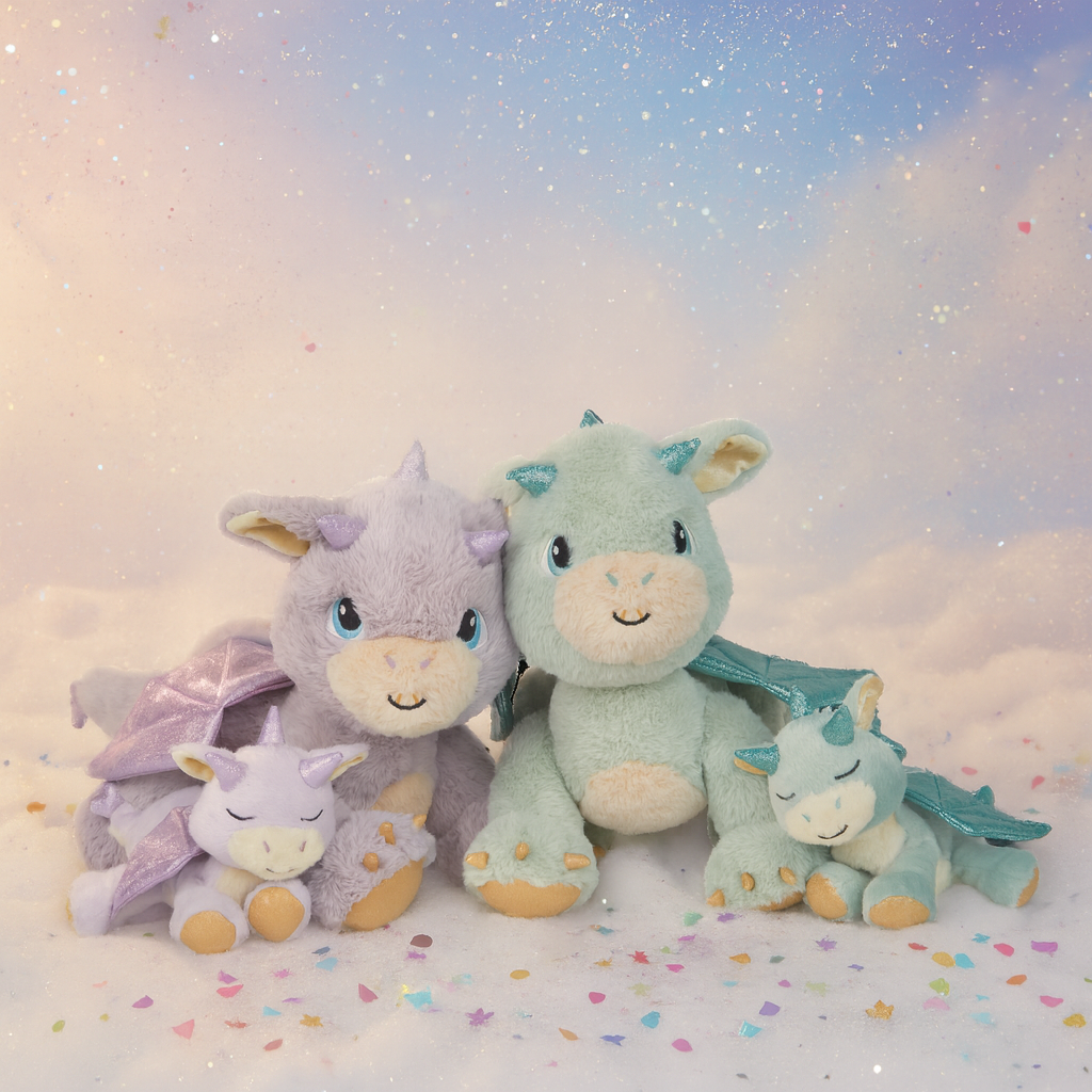 Four dragon-themed plush toys on a soft, cloud-like surface with a pastel sky background.