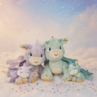 Four dragon-themed plush toys on a soft, cloud-like surface with a pastel sky background.